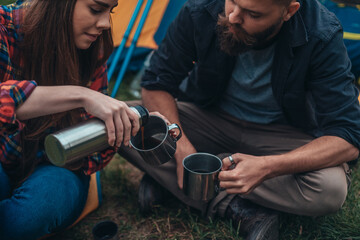 Couple of campers drinking coffee in the morning from a metal cups and thermos