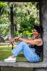 Mid adult afro mexican woman sitting in a park bench, smiling and looking at the camera