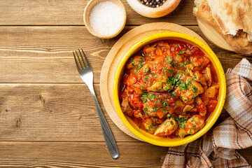 Traditional georgian dish Chakhokhbili. Chicken stew with tomatoes in ceramic bowl on wooden background.