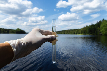 Scientist takes samples of dirty water from a pond. Hand is collects water in a test tube. Lake...