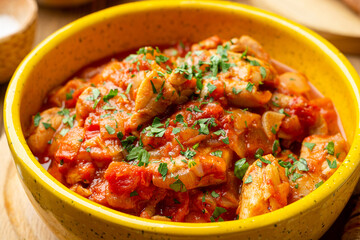 Traditional georgian dish Chakhokhbili. Chicken stew with tomatoes in ceramic bowl on wooden background.