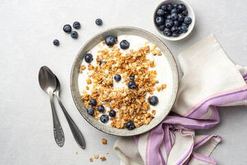 Yogurt with granola and blueberries in bowl on concrete background