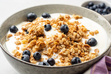 Yogurt with granola and blueberries in bowl on concrete background
