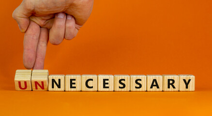 Necessary or unnecessary symbol. Businessman turns wooden cubes and changes the word Unnecessary to Necessary. Beautiful orange background, copy space. Business and necessary or unnecessary concept.
