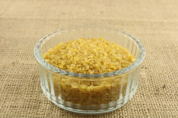 Uncooked coarse bulgur wheat in a glass bowl on a brown hessian background