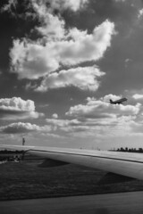 Naklejka na ściany i meble Planes taking off and wing of a plane at Narita International Airport in a cloudy day, Tokyo, Japan (in black and white)