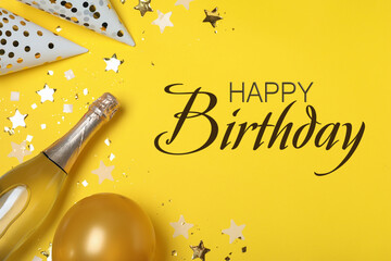 Happy Birthday! Flat lay composition with party decor and bottle of sparkling wine on yellow background