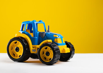 Children's toy blue yellow tractor on a yellow isolated background.