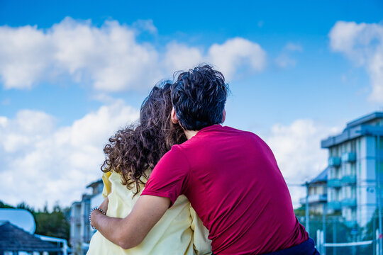 Coppia formata da un uomo e una donna abbracciata che guarda il cielo, ripresa da dietro con il cielo azzurro sullo sfondo. ottobre. italia. amore. abbraccio. autunno. felicit&agrave;. 