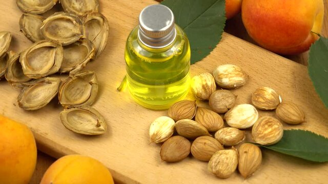 A bottle of the apricot kernel oil stands on a wooden board among the fresh apricots and the apricot kernels. Apricots and their products as a skin care product.
