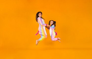 funny girls in plush pajamas jump on a yellow background with a place for text