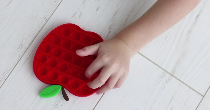 figers of toddler kid are pushing the bubbles on sensory toy, trendy pop it fidget toy in apple shape