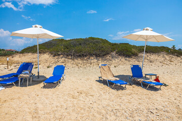 Landscape view of empty sunbeds under umbrellas on sand beach. Greece. 