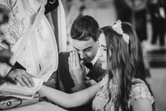 Stylish emotional bride and groom making oaths and holding hands on holy bible during matrimony in church. Wedding ceremony in cathedral. Classic wedding couple giving vows. Black and white image