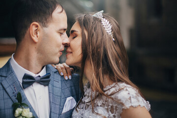 Portraits of stylish bride and groom kissing and embracing on background of old church. Romantic moment. Provence wedding. Beautiful sensual wedding couple gently hugging in european city