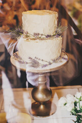 Stylish rustic wedding cake with lavender and thistle decor on vintage stand on table at wedding reception in restaurant. Modern beautiful provence wedding cake. Luxury catering at banquets