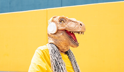 woman with with t-rex mask, and headphones listens to music on a yellow and blue wall
