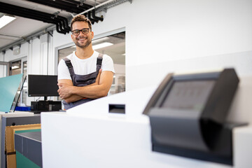 Portrait of smiling print worker standing by computer to plate machine in print shop.