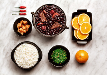 Ingredientes de feijoada sobre fundo de mármore - feijão, arroz, torresmo, couve, laranja e...