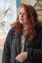 Young beautiful blue-eyed red-haired plump girl in autumn clothes outdoors.