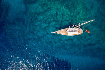 Aerial top down view to a sailing boat over the turquoise and emerald shining, mediterranean sea