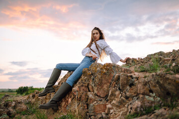 Naklejka na ściany i meble Young cheerful woman wearing cowgirl boots posing in the countryside. Fashion, style, lifestyle concept. Summer time.