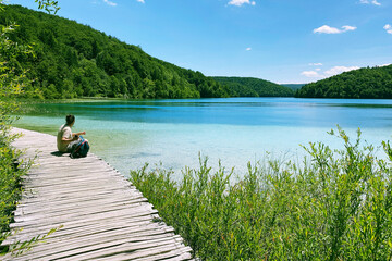 Tourist relaxing in nature. Summer landscapes along lake in traveling journey. Wooden vintage bridge walkway.