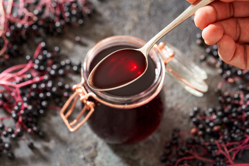 A spoon with black elder syrup made from fresh elderberries