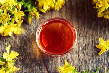 A bowl of red oil made from St. John's wort flower with fresh Hypericum plant