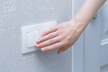 Close-up hand of caucasian woman turns on wall light switch in the room.