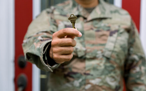 solider holding key in front of house