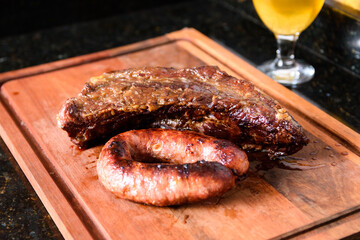 Close-up de um churrasco de bife e linguiça em uma tábua, no fundo um copo de cerveja. Churrasco tradicional do sul do brasil.