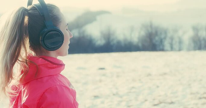 Running woman, headphone girl runner on the snow in winter sunny day. Female in pink sportswear jacket fitness training outdoors. Sport concept, leisure and freedom. 4K slow motion video 
