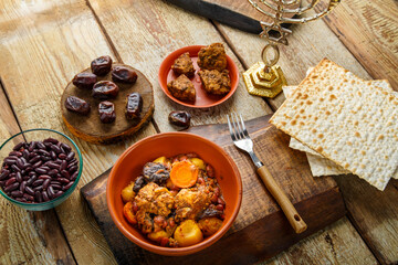 Jewish dish chelnt with meat on a stand next to matzo and ingredients.