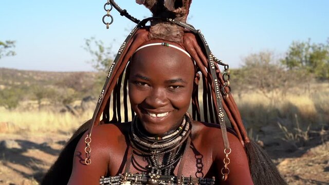 Beautiful young Himba woman smiling, wearing traditional jewellery and headdress in her village near Kamanjab in northern Namibia, Africa.