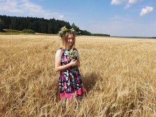 Naklejka na ściany i meble a girl in a dress and a wreath is standing in a field with a bouquet 