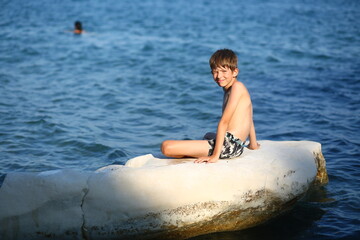 Caucasian nine year old boy sunbathing on the rocks on the cyprus seashore