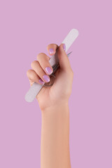Womans hand holding manicure instrument on pastel lavender background - obrazy, fototapety, plakaty