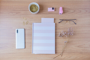 Workspace with pale pink and white stationary on wooden background. Flat lay, top view. Feminine desk concept.