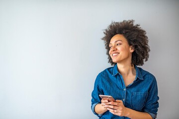 Smiling mature woman using smartphone isolated on gray wall with copy space. Happy African American woman in casual typing on cellphone over grey background.