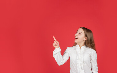 amazed child in white shirt pointing finger on red background copy space, advertisement