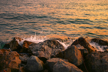 Sunset on a rocky stone beach. Orange sunset on the beach with big stones. Large stones with a beautiful texture against the background of a sea sunset. Evening landscape on the rocky sea shore.