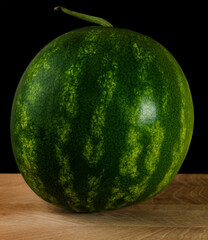 Whole watermelon on wood board on black background
