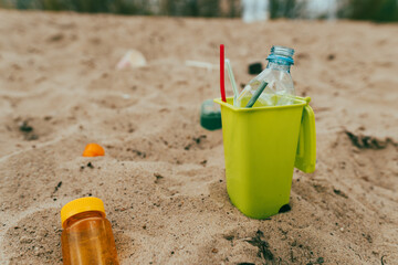 Small toy waste container on the sand beach with plastic garbage