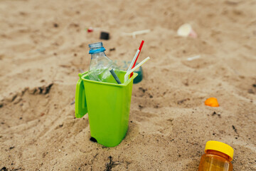 Small toy waste container on the sand beach with plastic garbage