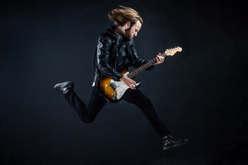 emotional bearded rock musician playing electric guitar in leather jacket and jumping, bas-guitar - obrazy, fototapety, plakaty