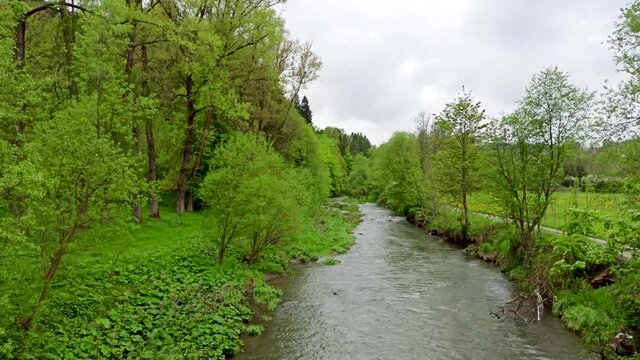 A river named klikuszowka flowing near Rabka Zaryte surrounded with greenery and trees against overcast clouds and rainy weather.