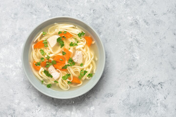 Homemade chicken soup with noodles and vegetables on a gray rustic background. Top view, flat lay, copy space.
