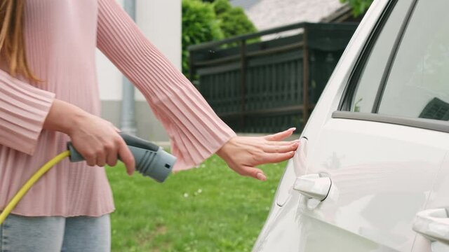 Handheld shot of a Caucasian woman putting a charging plug or charger in a white electric car
