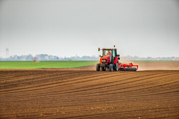 Obraz premium Farmer in tractor preparing land with seedbed cultivator as part of pre seeding activities in early spring season of agricultural works at farmlands.